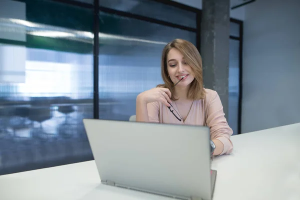 Jovem positiva trabalhando em um laptop no escritório e sorrindo. Trabalho em co-trabalho . — Fotografia de Stock