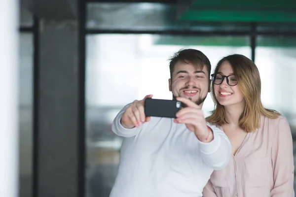 Улыбающиеся мужчина и девочка делают селфи в помещении. Пара офисных работников сделает селфи смартфоном. Счастливые сотрудники фотографируются на смартфоне в офисе . — стоковое фото
