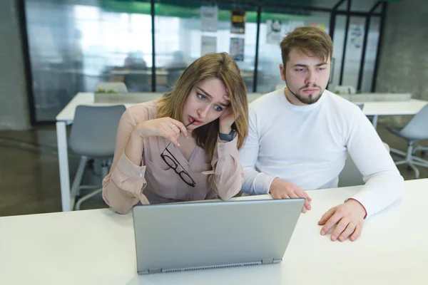 Sad young man and girl are sitting at a desk near a laptop in the office and are sad. Failure at work. Office work concept.
