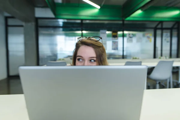 Empregada de escritório sentada no escritório no local de trabalho e escondida atrás de um laptop . — Fotografia de Stock