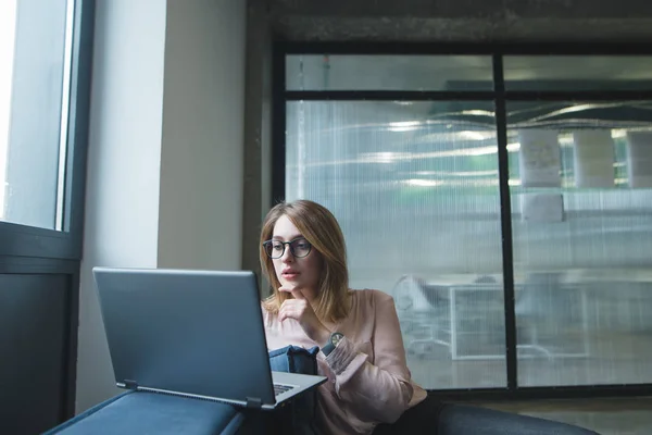 A vonzó lány a notebook, a háttérben a irodaterület néz. A lány szerkezet-ra egy laptop, egy kanapé, a háttérben az irodám falán. — Stock Fotó