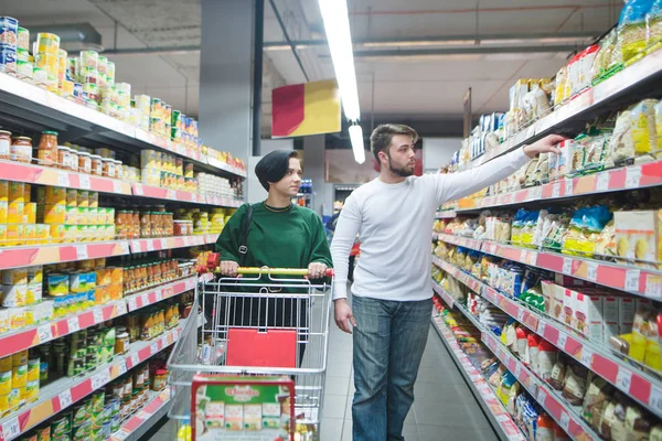 Молодая красивая пара, гуляющая с корзиной супермаркета и выбирающая товары. Семейные покупки в супермаркете — стоковое фото