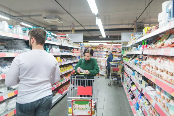 People shop at a supermarket. A girl walks through a supermarket, a man chooses goods from shelves. Shopping in a supermarket concept. — Stock Photo, Image