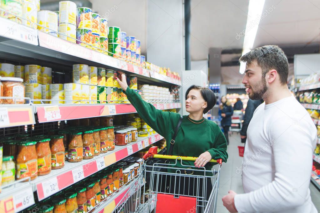 Young people with a cart choose canned vegetables in a supermarket. Family shopping at the store.