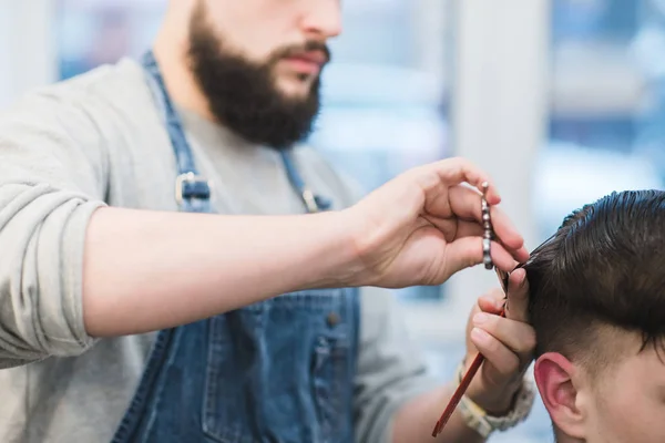 Barber with a beard cuts a customer with scissors. A man with a beard scissors cuts his hair. Men's haircuts in barbershop