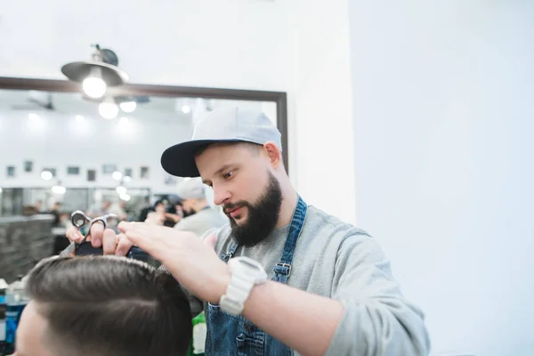 Barbier avec une barbe ciselant les ciseaux de son mari. Le mari d'un coiffeur fait une coiffure au client. Coupes de cheveux pour hommes chez le coiffeur — Photo