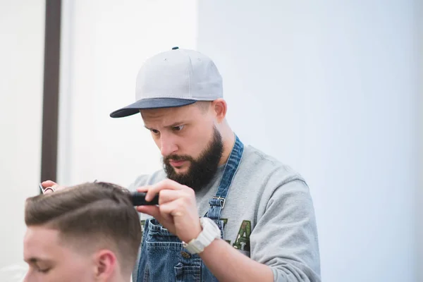 Porträt eines Friseurs bei der Arbeit. Friseur mit Mütze erwischt den Kunden im Friseursalon mit der Schere. Männerfrisuren — Stockfoto