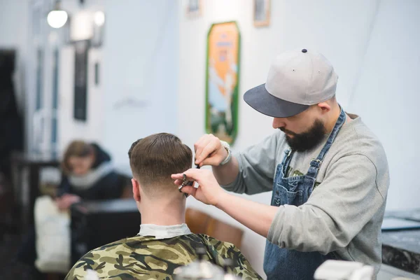 Haarschnitt im Friseurladen. Der männliche Friseur mit Bart macht dem Kunden eine Frisur. Friseur schneidet jungen Mann im Friseursalon eines Mannes — Stockfoto