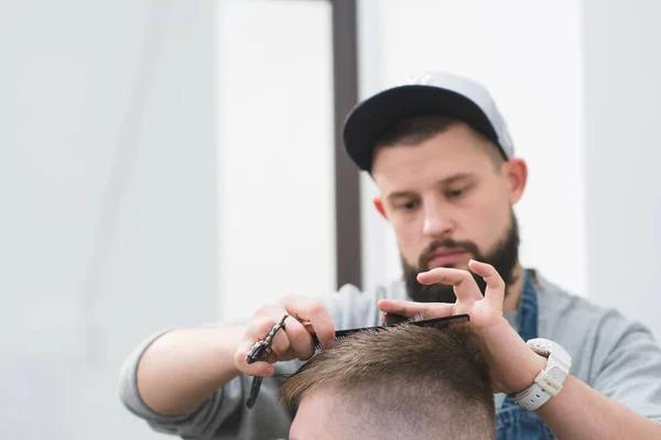 Corte de cabelo masculino na barbearia. Master Barber cria um penteado masculino elegante. Tesoura e cabelo em foco . — Fotografia de Stock