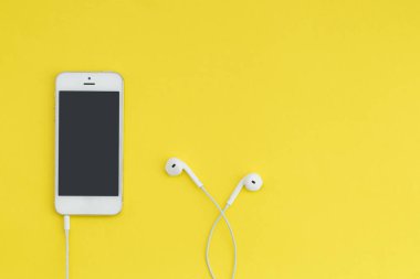 Karanlık bir ekran ve sarı bir arka plan üzerinde beyaz kulaklık ile smartphone. Lay kompozisyon düz. Müzik dinlemek.