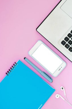 Düzeni ile bir dizüstü bilgisayar, telefon, not defteri ve pembe bir arka plan üzerinde kulaklık. Metin için yer. Çalışmaya Lay şeyler düz
