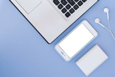Dizüstü bilgisayar, telefon, kulaklık ve güç üzerinde mavi bir arka plan banka. Düz yatıyordu kompozisyon ve metin için yer. Üstten Görünüm.