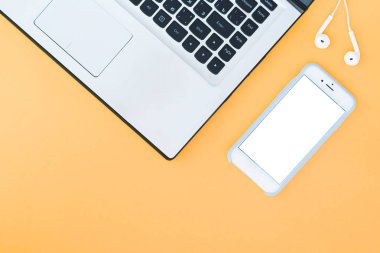 Laptop ve beyaz bir ekran ve turuncu zemin üzerine kulaklıklar sahip. Minimalist çalışma alanı ile metin için bir yer. Düz Lay