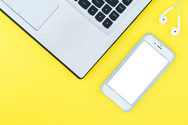 Laptop ve beyaz bir ekran ve kulaklıktan sarı arka plana sahip. Minimalist çalışma alanı ile metin için bir yer. Düz Lay