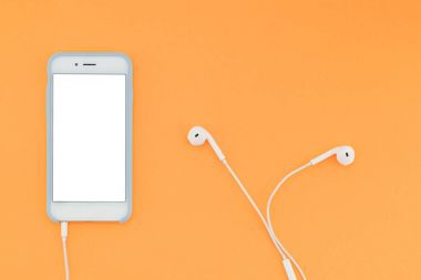 Beyaz bir ekran ve turuncu arka plan üzerinde kulaklık ile smartphone. Üstten Görünüm. Düz yatıyordu.