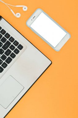 Laptop ve beyaz bir ekran ve turuncu zemin üzerine kulaklıklar sahip. Minimalist çalışma alanı ile metin için bir yer. Düz Lay
