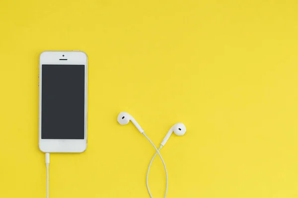 Смартфон с темным экраном и белыми наушниками на желтом фоне. Плоская композиция. Слушать музыку . — стоковое фото