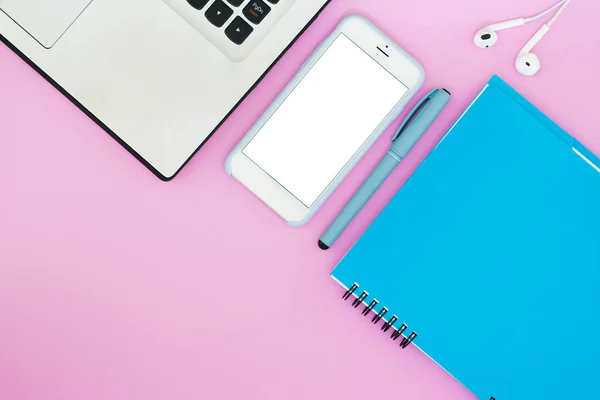 Lay-out met een laptop, telefoon, Kladblok en koptelefoon op een roze achtergrond. Plek voor tekst. Plat lag dingen om te werken. — Stockfoto