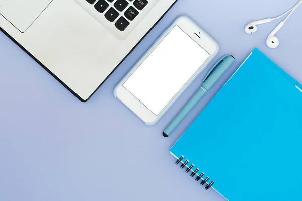Diseño con un ordenador portátil, teléfono, bloc de notas y auriculares sobre un fondo azul. Lugar para el texto. Diseño plano de herramientas de escritorio . — Foto de Stock