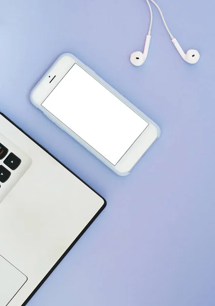 Un teléfono con una pantalla blanca, un ordenador portátil y auriculares sobre un fondo azul. Gadgets de posición plana y lugar para texto . — Foto de Stock