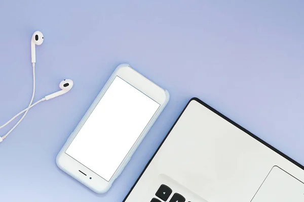 Телефон с белым экраном, ноутбук и наушники на синем фоне. Плоские устройства Lay и место для текста — стоковое фото