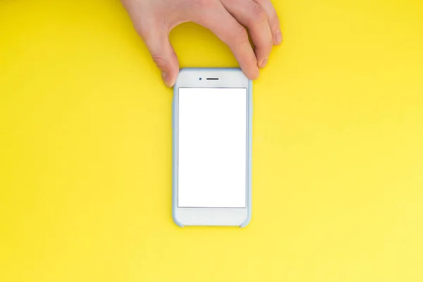 Mano plana con teléfono. La mano sostiene un teléfono inteligente con una pantalla blanca sobre un fondo amarillo. Mano con teléfono aislado sobre fondo amarillo . — Foto de Stock