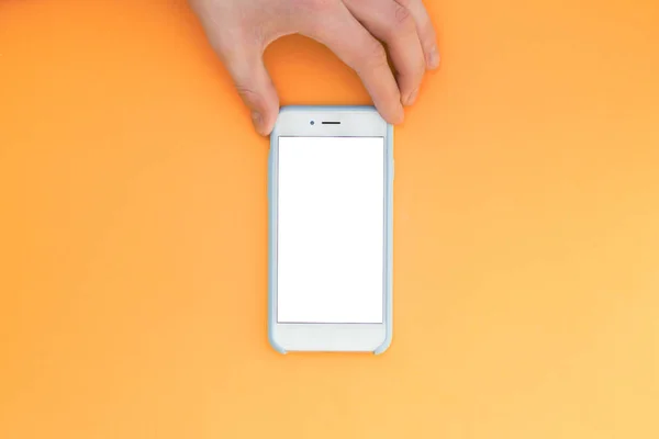 Flat lay hand with phone. The hand holds a smartphone with a white screen on top of a orange background. Hand with phone isolated on yellow background