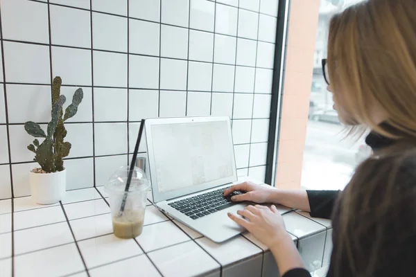 Дівчина працює на ноутбук у стильному легкому кафе і п'є сонечко. Студент, який навчається за комп'ютером у кафе — стокове фото