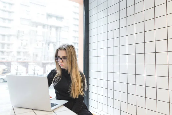 Uma bela estudante desfruta de um nerd em um laptop em um café design elegante, moderno e leve. Trabalho em um café para um computador — Fotografia de Stock