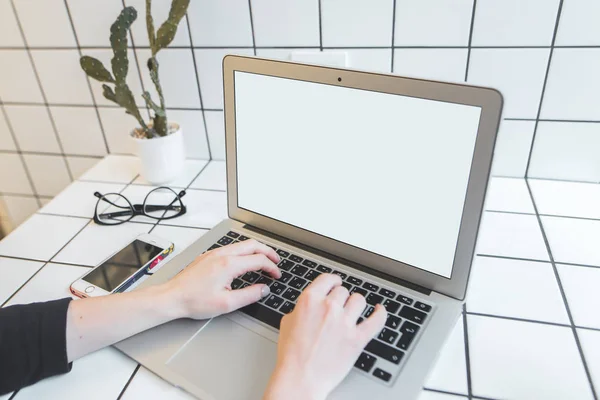 Uno studente lavora per un portatile in un bar. La ragazza digita il testo su un computer portatile con un monitor bianco al tavolo elegante nel caffè . — Foto Stock