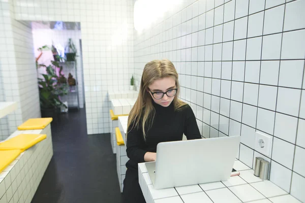 Молода дівчина працює як комп'ютер у ресторані зі світлим сучасним інтер'єром. Робота фрілансера в кафе на ноутбуці . — стокове фото