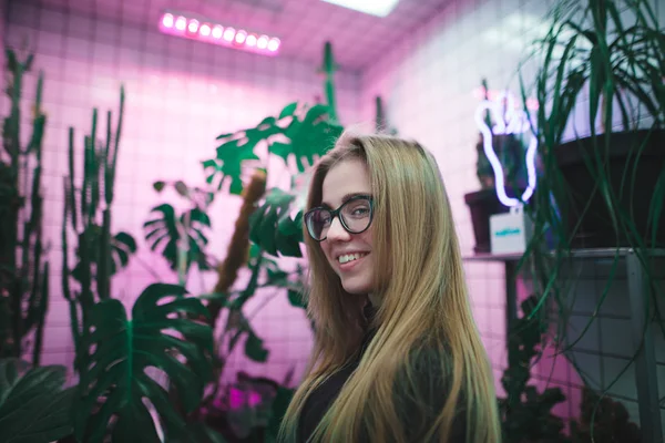 Een lachende jong meisje met zich meebrengt in een kamer met violet licht en groene planten — Stockfoto
