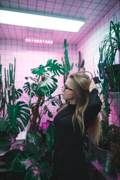 Hermosa joven posando en una habitación con luz violeta y jarrones verdes . —  Fotos de Stock