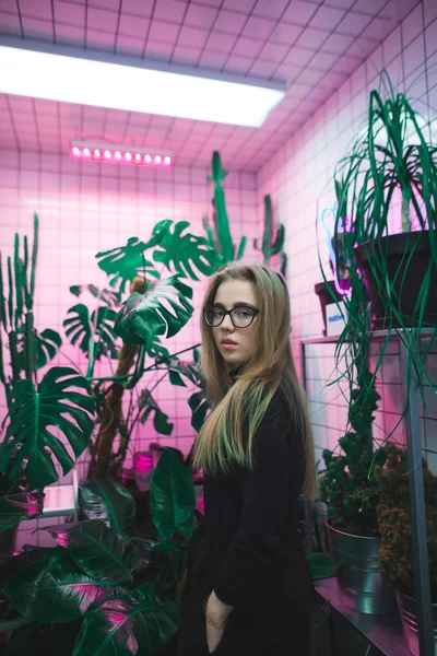 Retrato de uma bela jovem em um quarto com luz violeta néon e vasos . — Fotografia de Stock