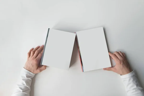 Hände halten weiße Bücher auf hellem Hintergrund. weiße Bücher mit Händen auf einem weißen Tisch. flache Lage. — Stockfoto