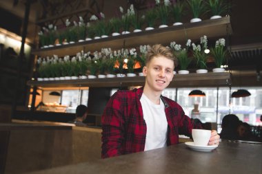 Pozitif genç adam ile bir fincan kahve ve gülümser bir kafede oturuyor. Kafede kahve