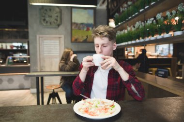 Genç adam rahat bir kafede yemek yerken kahve içme zevk ile. Bir öğrenci kahve içer ve bir salata yiyor. Öğle yemeği molası.