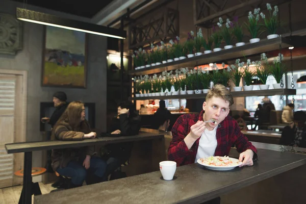Un joven come una ensalada en un restaurante acogedor. Los platos de los estudiantes y el café en la cafetería . — Foto de Stock