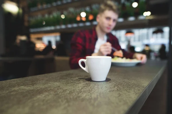 Šálek horkého nápoje na pozadí osoby, která jí restaurace — Stock fotografie