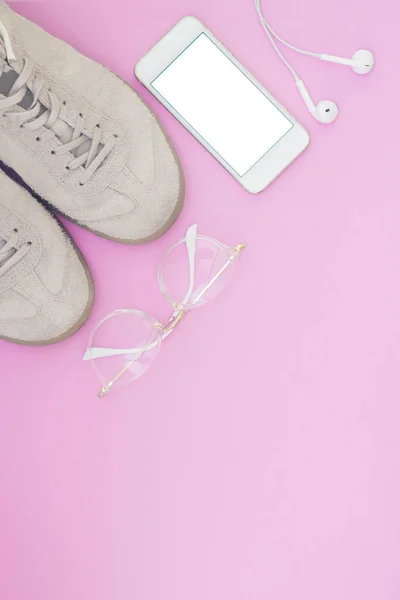 Sneakers, phone, glasses and headphones on the pink pastel backg