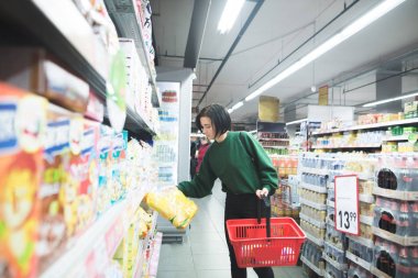 Kız süpermarket raf kuru kahvaltılar bir paket alır. Bir alıcı bir sepet ile bir süpermarkette alışveriş yapar.