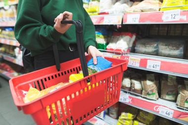 Kadın alışveriş sepetindeki ürünler koyar. Bir süpermarkette alışveriş. Kırmızı alışveriş sepetindeki ürünleri.
