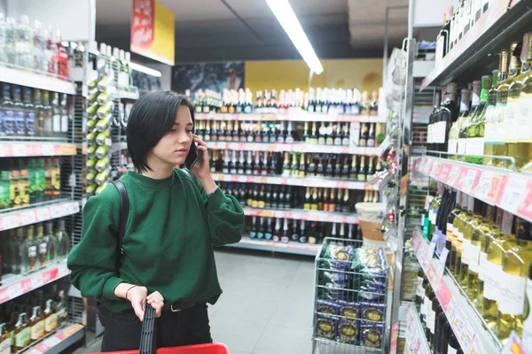 Девушка звонит по телефону и выбирает продукты в супермаркете . — стоковое фото