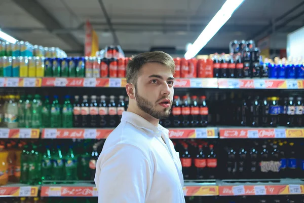 Retrato de un joven con un fondo de bebidas refrescantes en un supermercado . — Foto de Stock