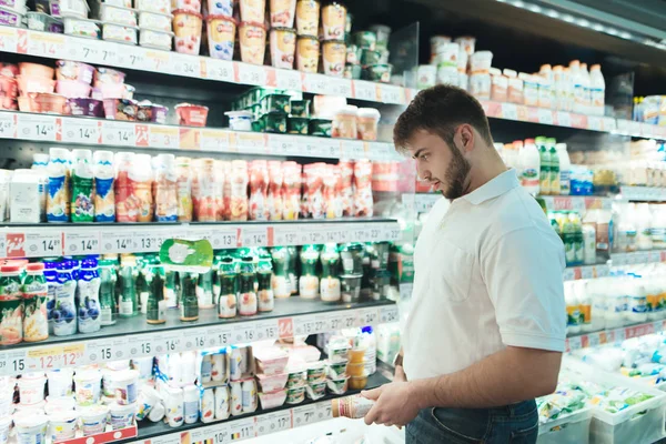Ένας άνθρωπος επιλέγει γιαούρτι σε ένα σούπερ μάρκετ. Ο αγοραστής επιλέγει γαλακτοκομικά προϊόντα. στο κατάστημα. Ένας άνδρας αγοράζει τροφίμων σε ένα σούπερ μάρκετ. — Φωτογραφία Αρχείου