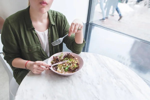 A girl eating a salad in a light restaurant at the table near the window. Healthy eating at the restaurant.