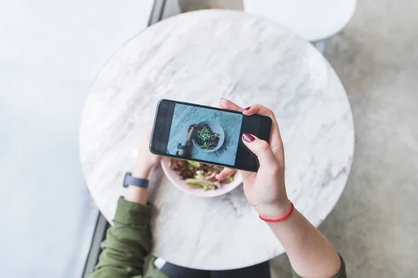Eine Frau macht ein Foto von ihrem Essen im Restaurant am Tisch. Der Blogger holt sich einen Salat am Tisch. — Stockfoto