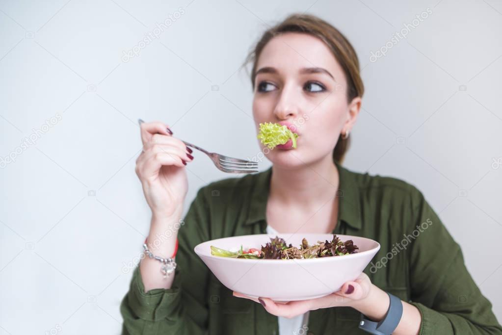 A funny woman eating salad greens. Cute girl with a plate of salad in their hands. Healthy eating and healthy food. Focus on food.