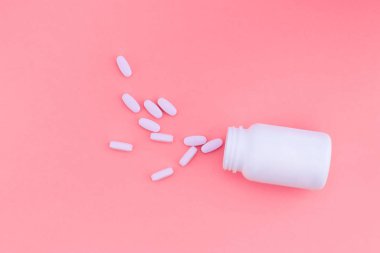 Hapları bir kavanozdan pembe bir arka plan üzerine dökülür. Vitaminler parlak pembe bir arka plan üzerinde. Üstten Görünüm. Düz Lay