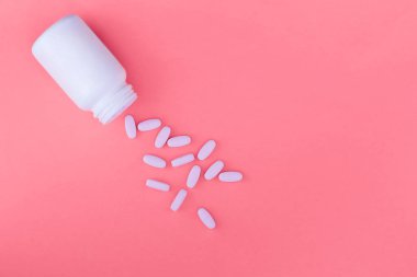 Bir şişe ilaç ve pastel pembe bir arka plan üzerinde dağınık hapları. Vitaminler parlak bir arka plan üzerinde yırtık. Düz yatıyordu Üstten Görünüm